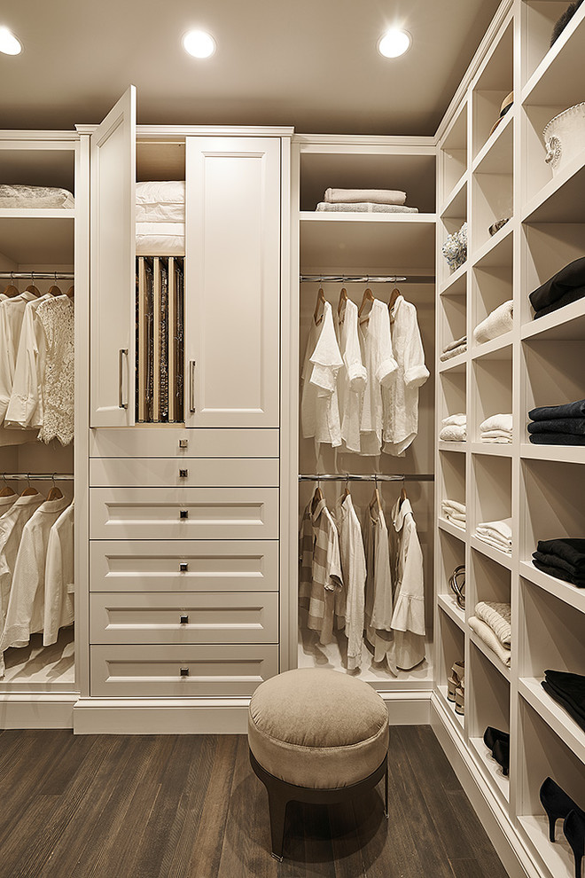 Modelo de armario vestidor unisex tradicional renovado de tamaño medio con armarios con paneles empotrados, puertas de armario blancas, suelo de madera oscura y suelo marrón