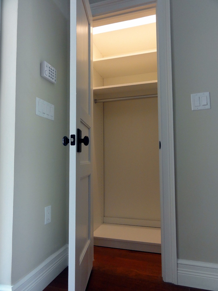 Foto de armario unisex tradicional renovado pequeño con armarios con paneles empotrados, puertas de armario blancas y suelo de madera en tonos medios