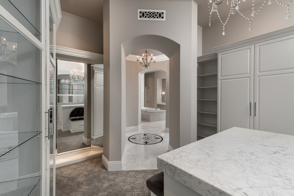 This is an example of a large mediterranean dressing room for women in Phoenix with glass-front cabinets, white cabinets, carpet and grey floors.