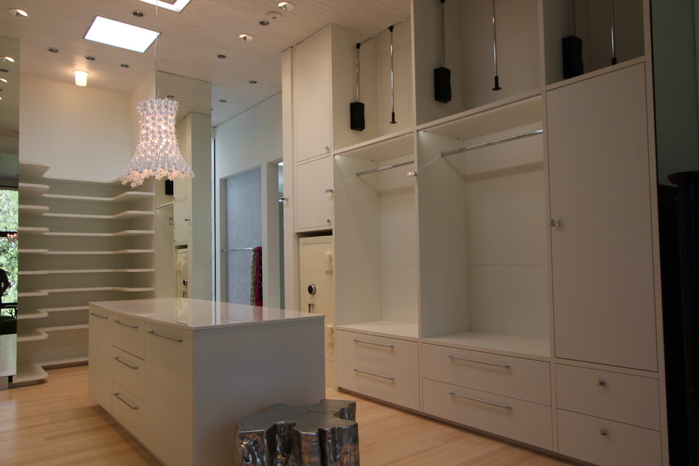 Modelo de vestidor unisex actual grande con armarios con paneles lisos, puertas de armario blancas y suelo de madera clara