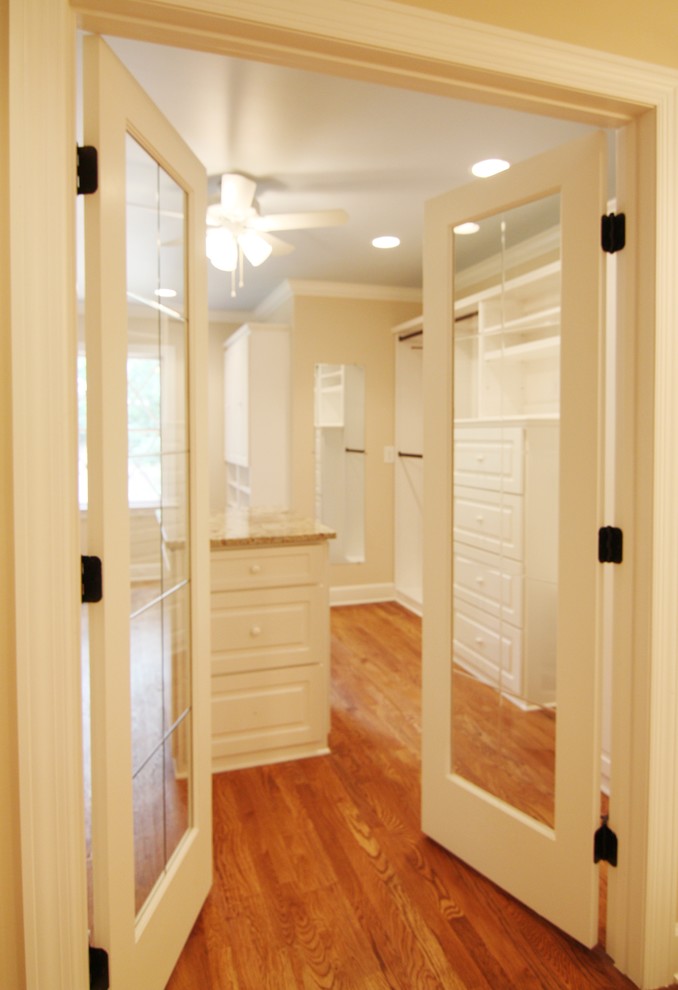 Modelo de vestidor unisex tradicional grande con armarios con paneles con relieve, puertas de armario blancas y suelo de madera en tonos medios