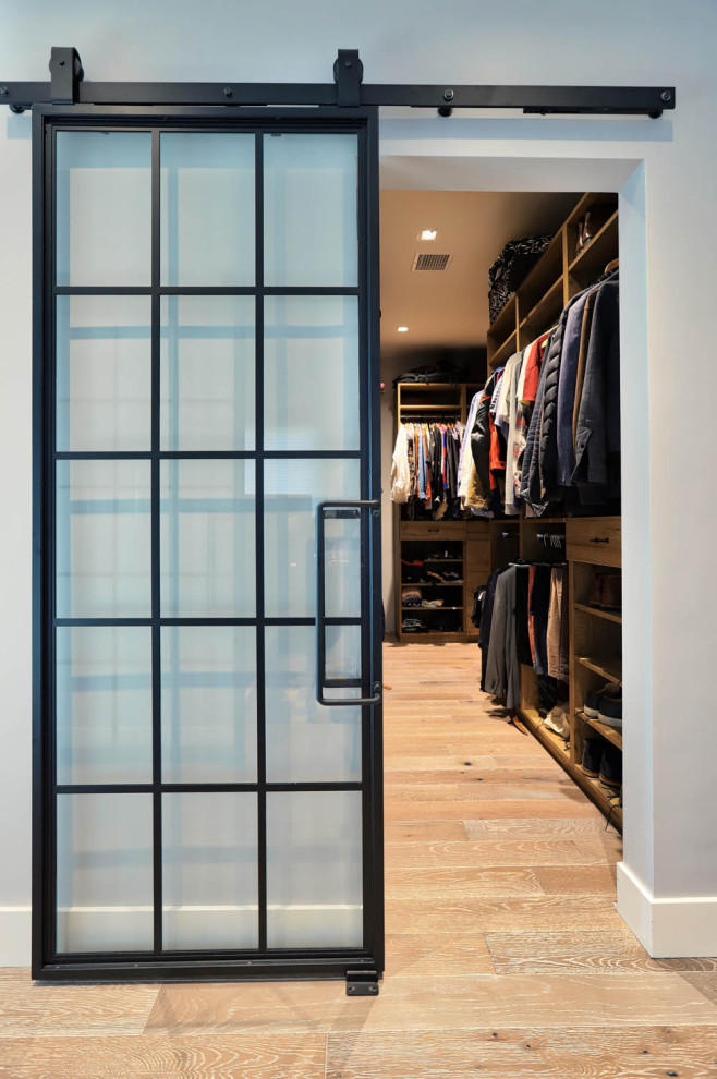 Diseño de armario vestidor unisex industrial grande con armarios con paneles lisos, puertas de armario de madera oscura, suelo de madera clara y suelo beige