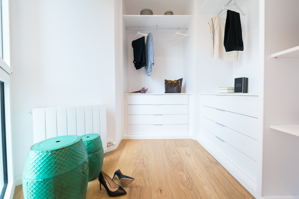 Modelo de armario vestidor de mujer escandinavo de tamaño medio con puertas de armario blancas, armarios con paneles lisos y suelo de madera clara