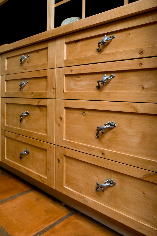 Diseño de armario y vestidor unisex bohemio con armarios estilo shaker, puertas de armario de madera clara y suelo de baldosas de terracota