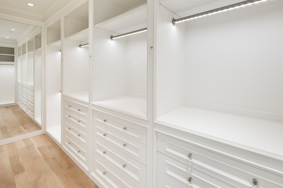 Imagen de armario vestidor unisex clásico renovado grande con puertas de armario blancas, suelo de madera clara y armarios con paneles empotrados