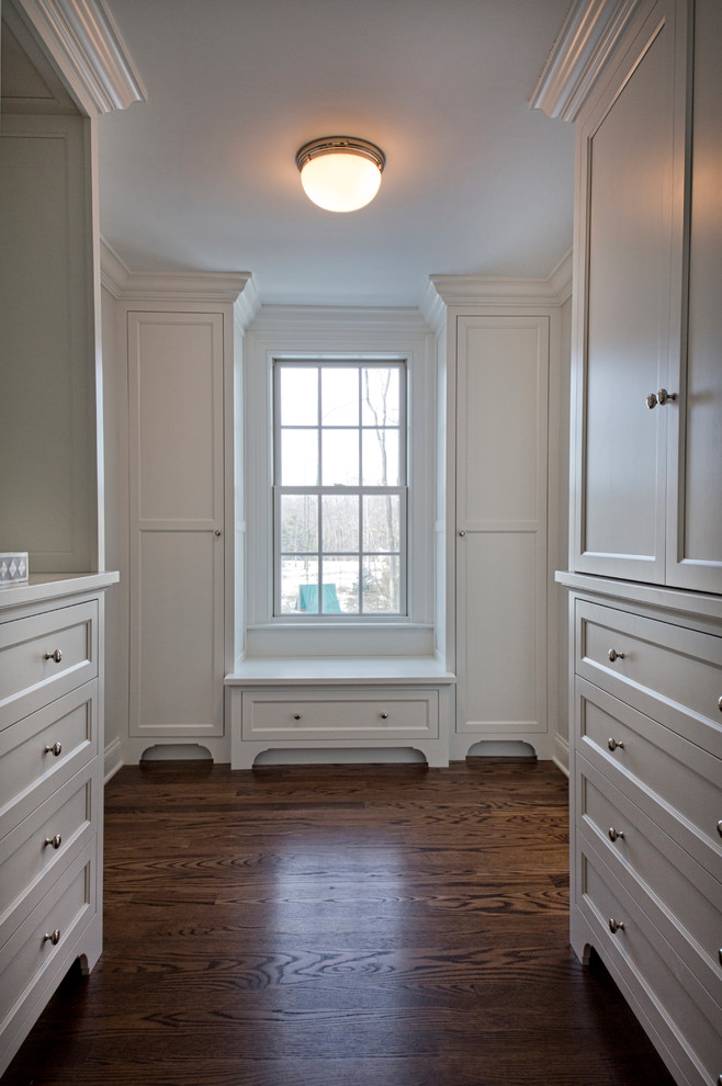 Klassisk inredning av ett walk-in-closet för könsneutrala, med luckor med infälld panel, vita skåp, mörkt trägolv och brunt golv