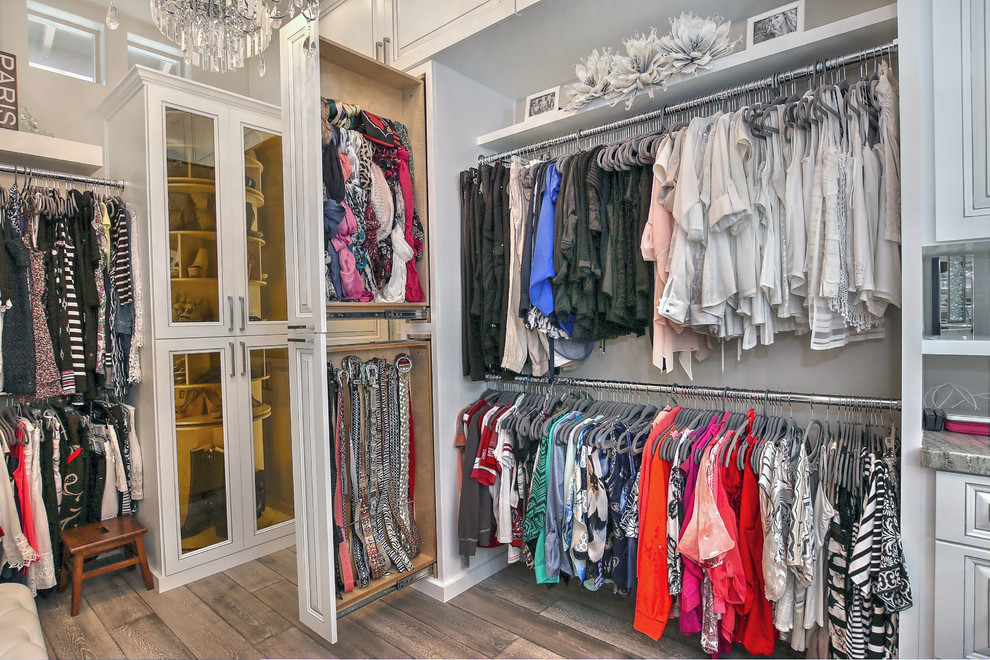 This is an example of a large modern walk-in wardrobe for women in Phoenix with glass-front cabinets, white cabinets, ceramic flooring and brown floors.
