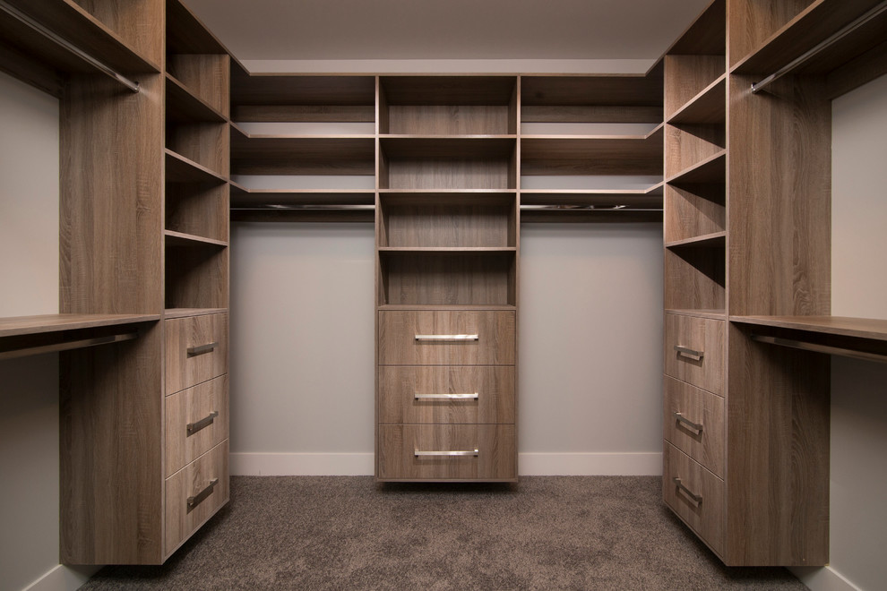 Imagen de armario vestidor unisex actual de tamaño medio con armarios con paneles lisos, puertas de armario de madera oscura y moqueta