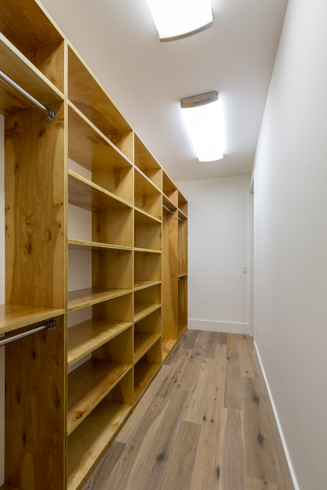 This is an example of a medium sized modern gender neutral walk-in wardrobe in Austin with open cabinets, light wood cabinets and medium hardwood flooring.