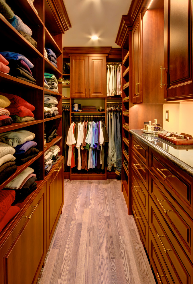 Immagine di una cabina armadio per uomo classica di medie dimensioni con ante con bugna sagomata, ante in legno bruno, pavimento in legno massello medio e pavimento marrone