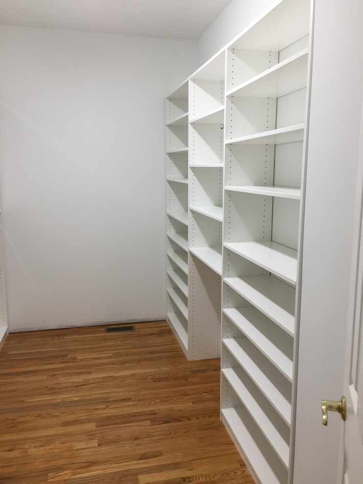 This is an example of a medium sized traditional gender neutral walk-in wardrobe in Other with white cabinets, medium hardwood flooring and brown floors.