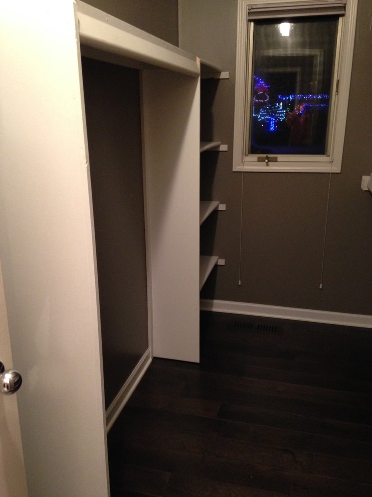 This is an example of a medium sized contemporary gender neutral walk-in wardrobe in Detroit with white cabinets and dark hardwood flooring.