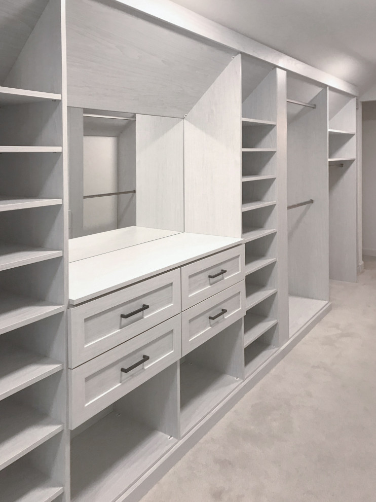 This is an example of an expansive classic walk-in wardrobe for women with recessed-panel cabinets, light wood cabinets, carpet and beige floors.