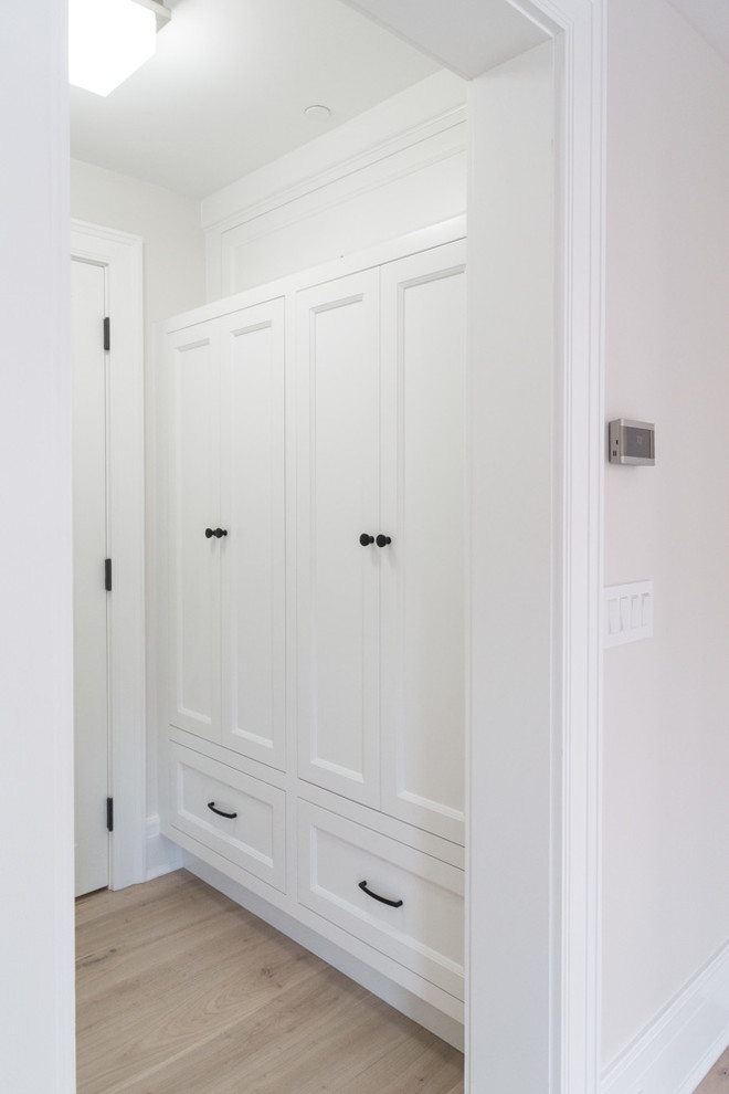 Diseño de armario vestidor unisex tradicional renovado de tamaño medio con armarios con paneles empotrados, puertas de armario blancas, suelo de madera clara y suelo beige