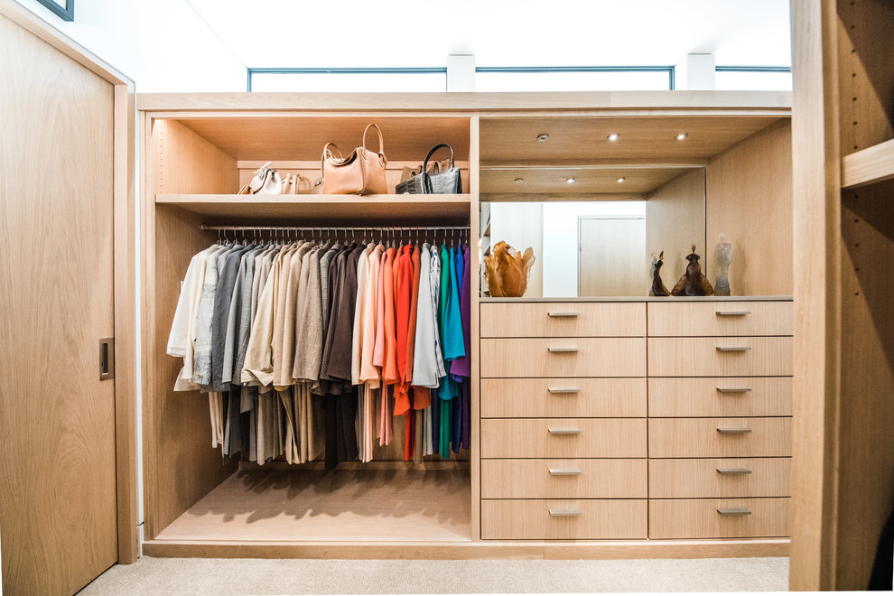 Diseño de armario vestidor unisex contemporáneo grande con armarios con paneles lisos, puertas de armario de madera clara, moqueta y suelo beige
