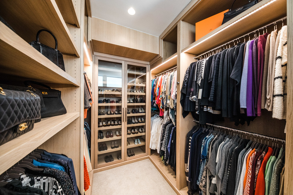 Ejemplo de armario vestidor unisex actual grande con armarios con paneles lisos, puertas de armario de madera clara, moqueta y suelo beige