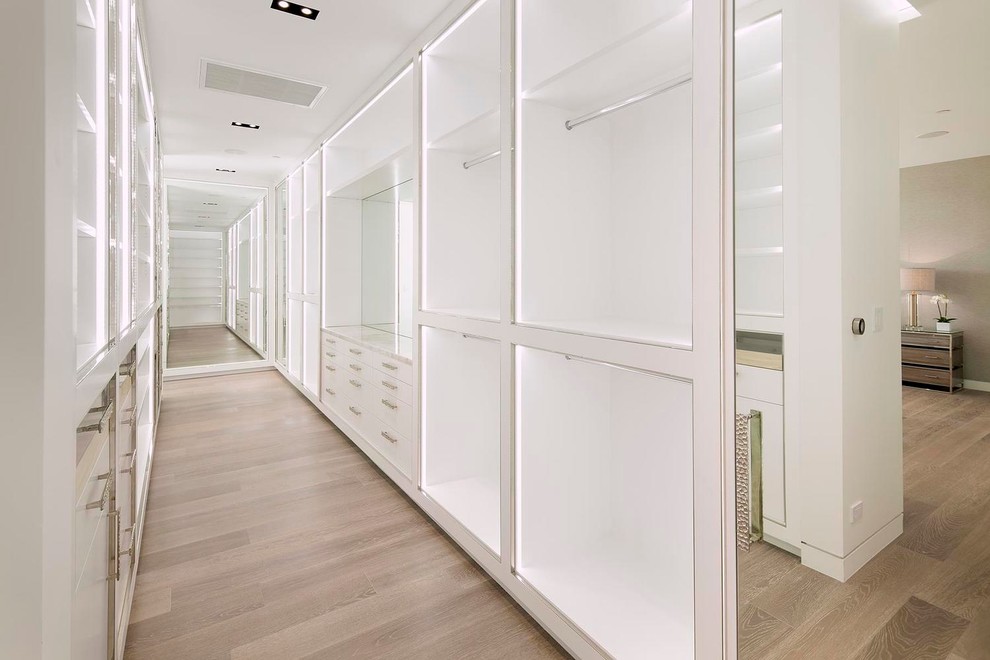 Idee per un'ampia cabina armadio per donna design con ante di vetro, ante bianche e pavimento in legno massello medio