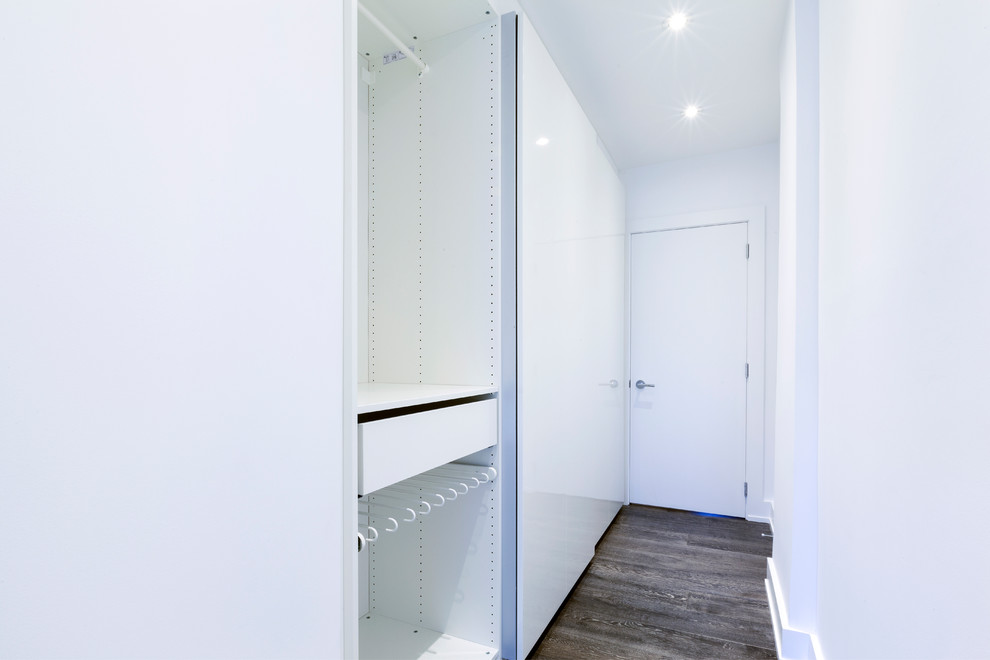 Exemple d'un placard dressing moderne de taille moyenne avec un placard à porte plane, des portes de placard blanches, parquet foncé et un sol marron.