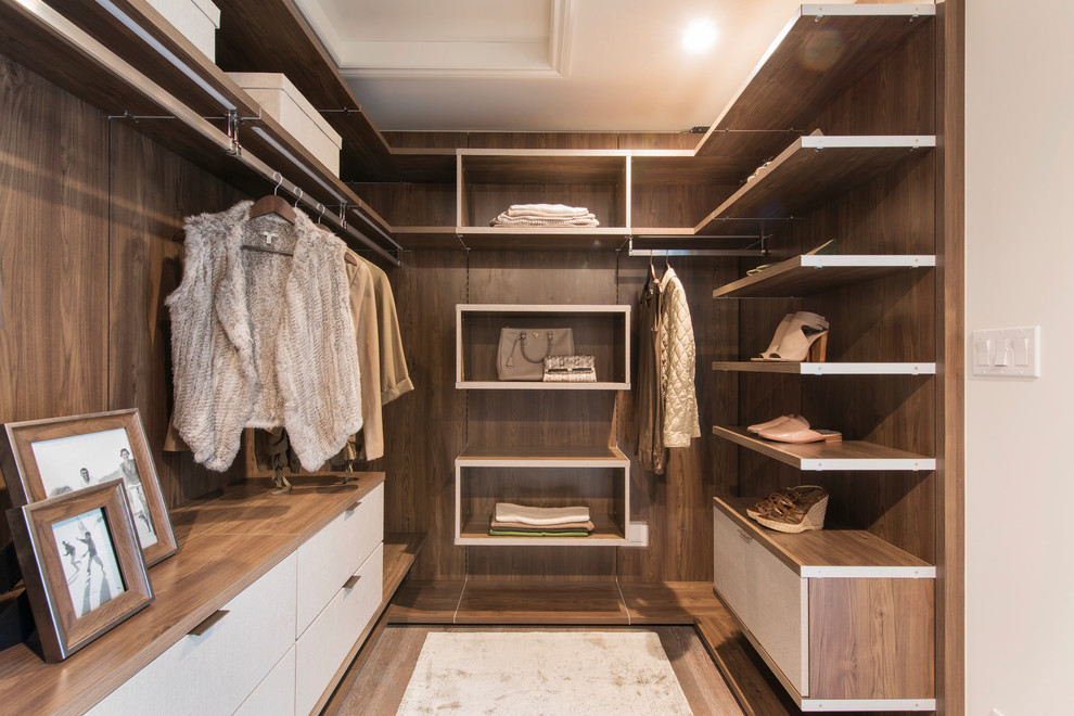Diseño de armario vestidor actual con armarios con paneles lisos, puertas de armario de madera oscura, suelo de madera en tonos medios y suelo marrón