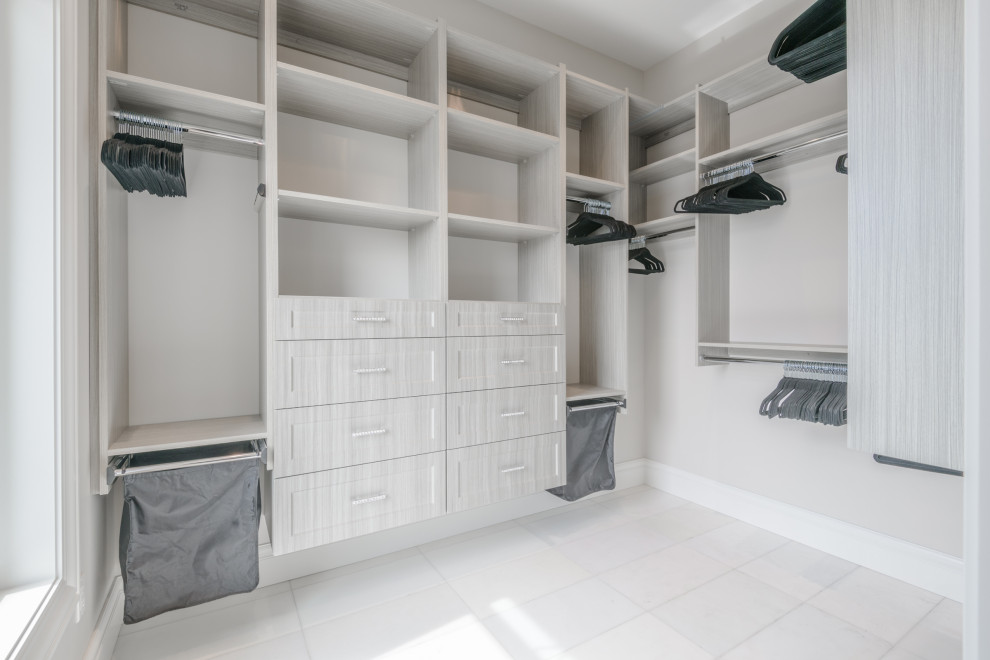 Diseño de armario vestidor unisex actual de tamaño medio con armarios con paneles empotrados, puertas de armario de madera clara, suelo de baldosas de porcelana y suelo blanco