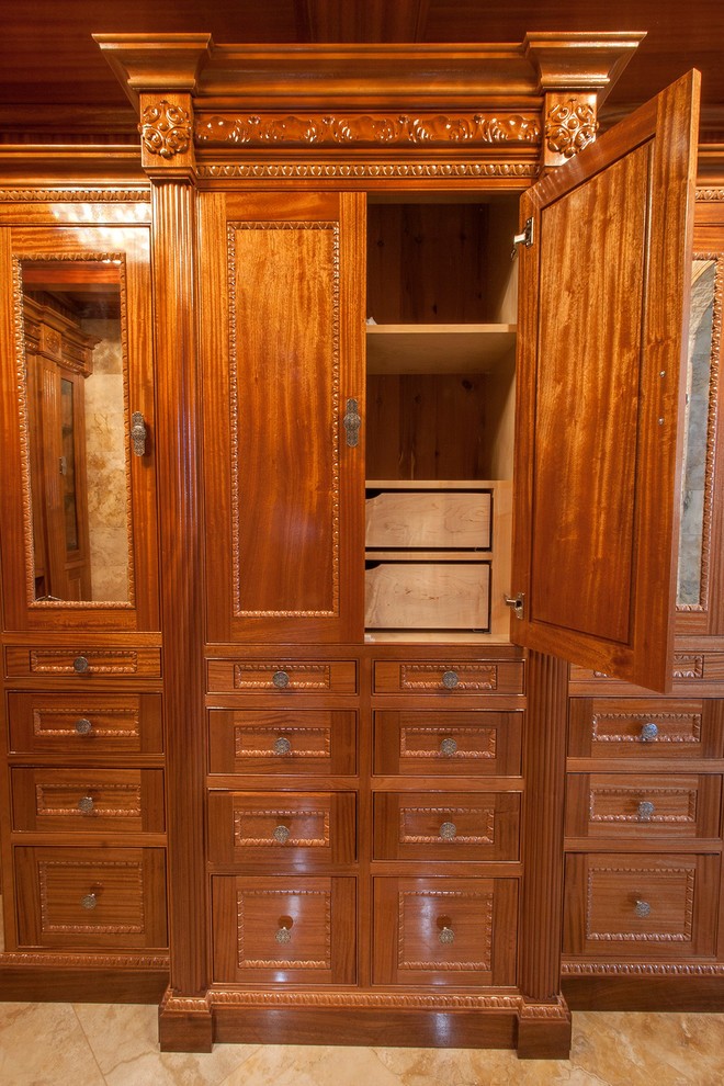Immagine di una grande cabina armadio unisex chic con ante a filo, ante in legno scuro e pavimento in travertino