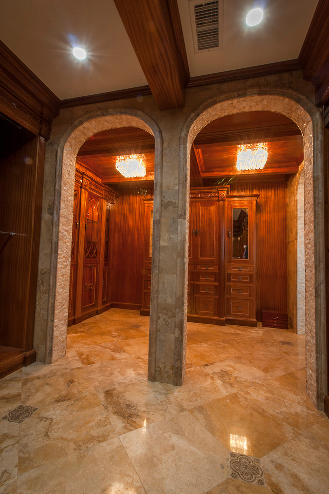 На фото: огромная гардеробная комната унисекс в классическом стиле с фасадами цвета дерева среднего тона и полом из травертина с