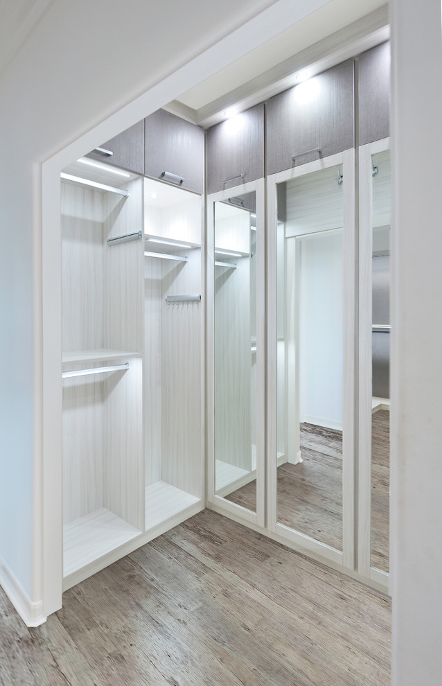Example of a mid-sized beach style gender-neutral light wood floor and brown floor walk-in closet design in Orange County with glass-front cabinets and white cabinets
