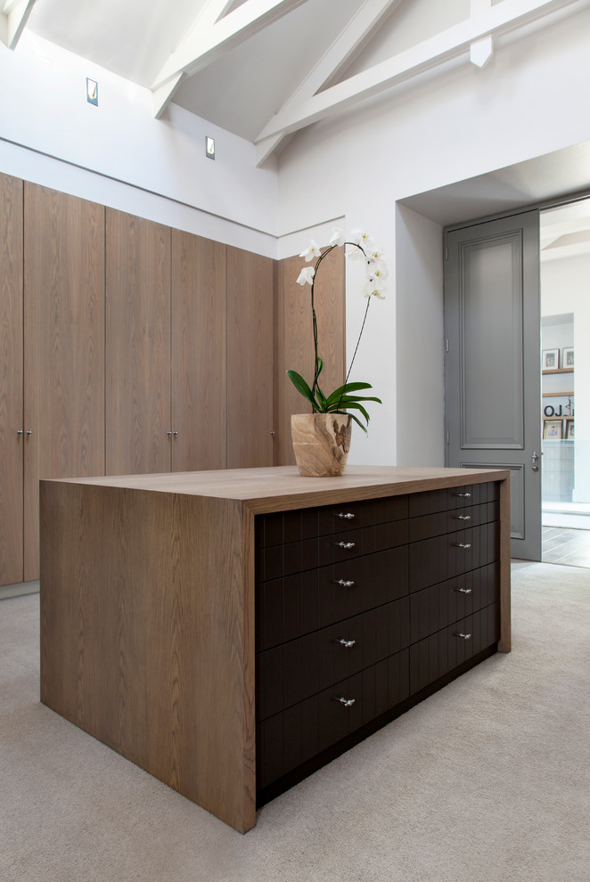 Photo of a contemporary gender neutral walk-in wardrobe in Other with flat-panel cabinets, medium wood cabinets, carpet and beige floors.