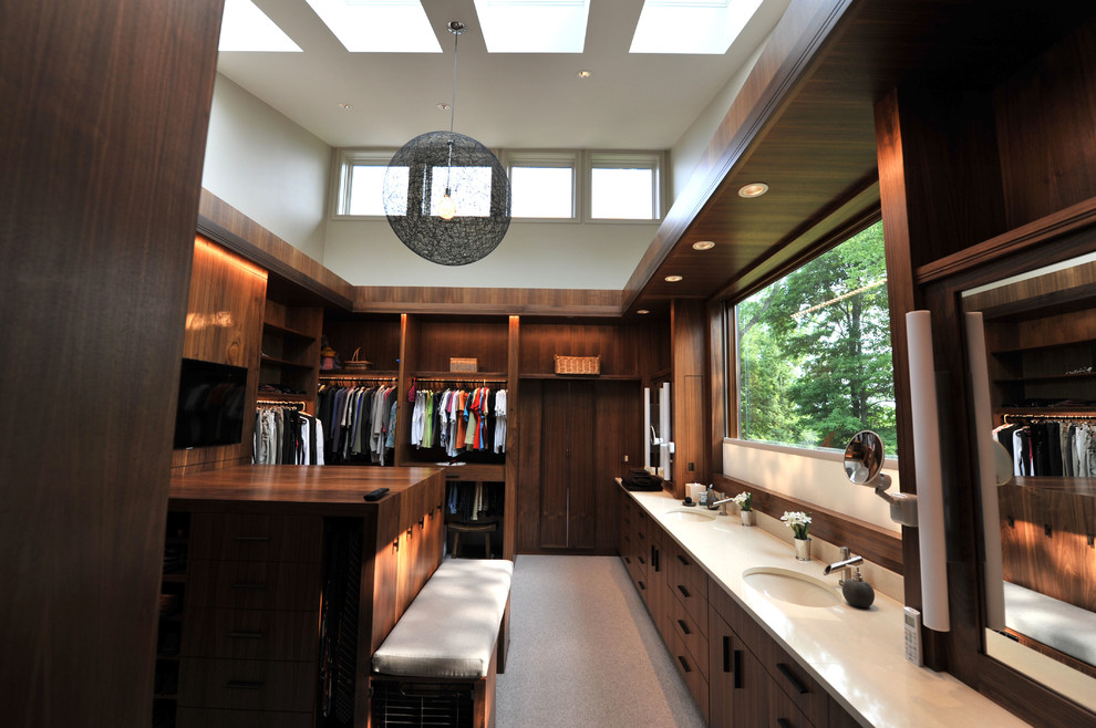 This is an example of an expansive contemporary gender neutral walk-in wardrobe in Cincinnati with flat-panel cabinets, medium wood cabinets, carpet and brown floors.