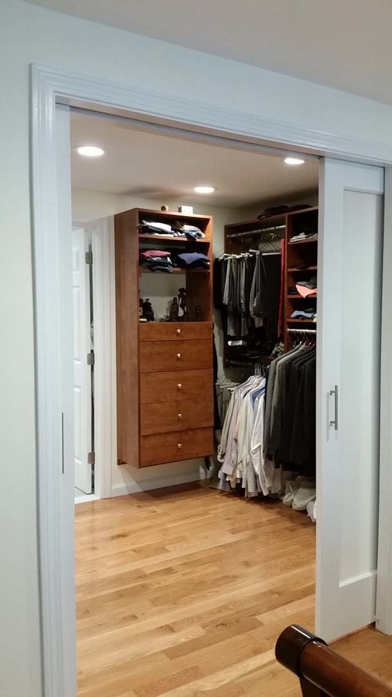 Modelo de armario vestidor unisex tradicional de tamaño medio con armarios con paneles lisos, puertas de armario de madera oscura y suelo de madera clara