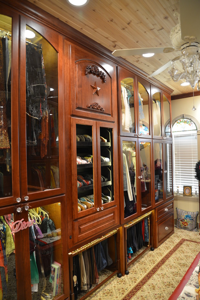 Example of a huge arts and crafts gender-neutral carpeted walk-in closet design in Houston with glass-front cabinets and medium tone wood cabinets