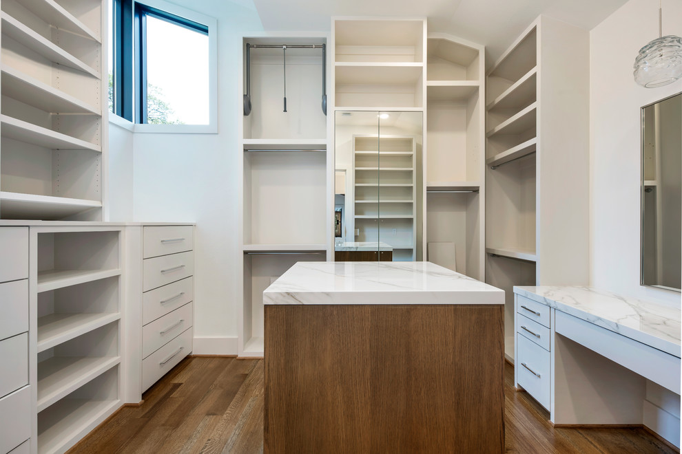 Modelo de armario vestidor unisex minimalista grande con armarios con paneles lisos, puertas de armario blancas, suelo de madera en tonos medios y suelo marrón