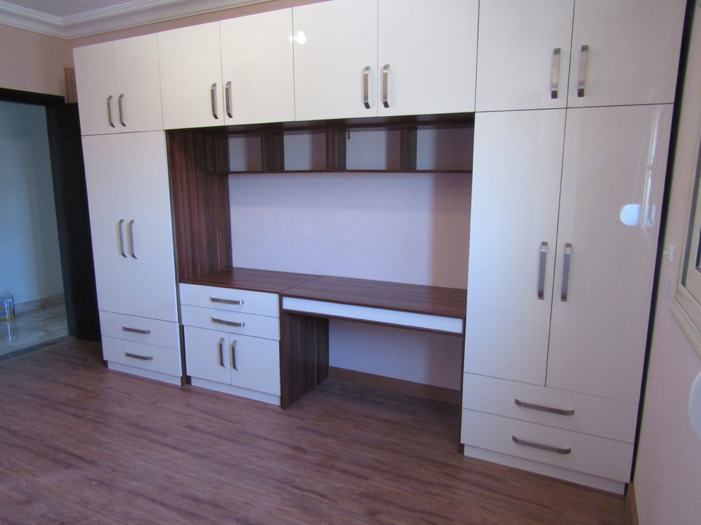 Imagen de armario unisex minimalista grande con armarios con paneles lisos, puertas de armario beige, suelo laminado y suelo marrón