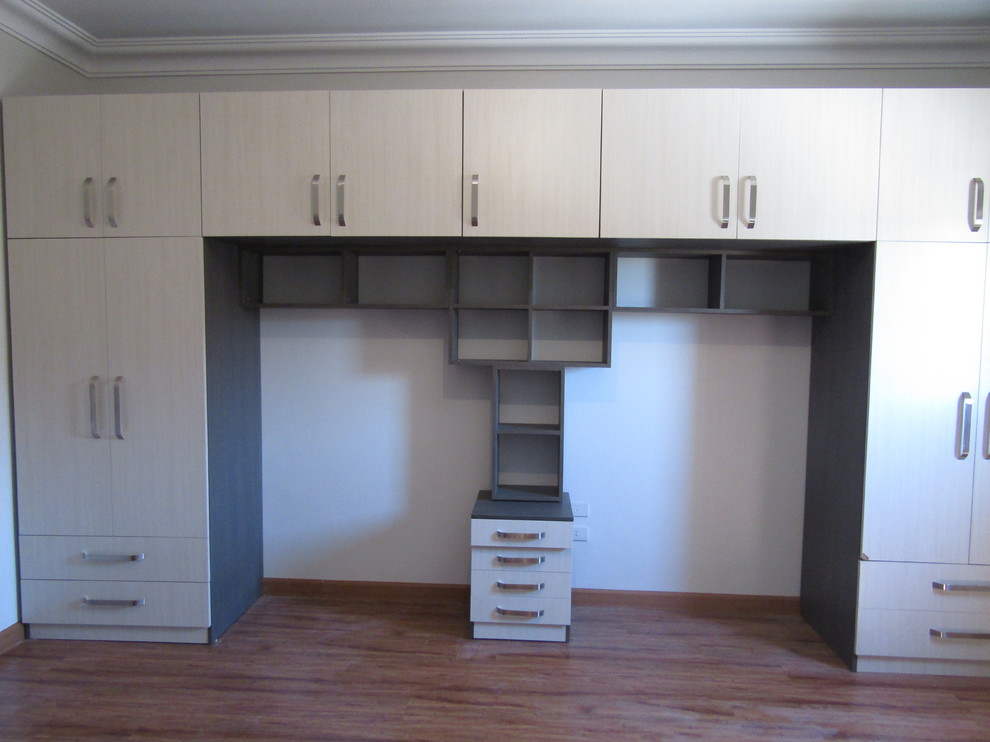 Inspiration for a large modern gender neutral standard wardrobe in Other with flat-panel cabinets, beige cabinets, laminate floors and brown floors.