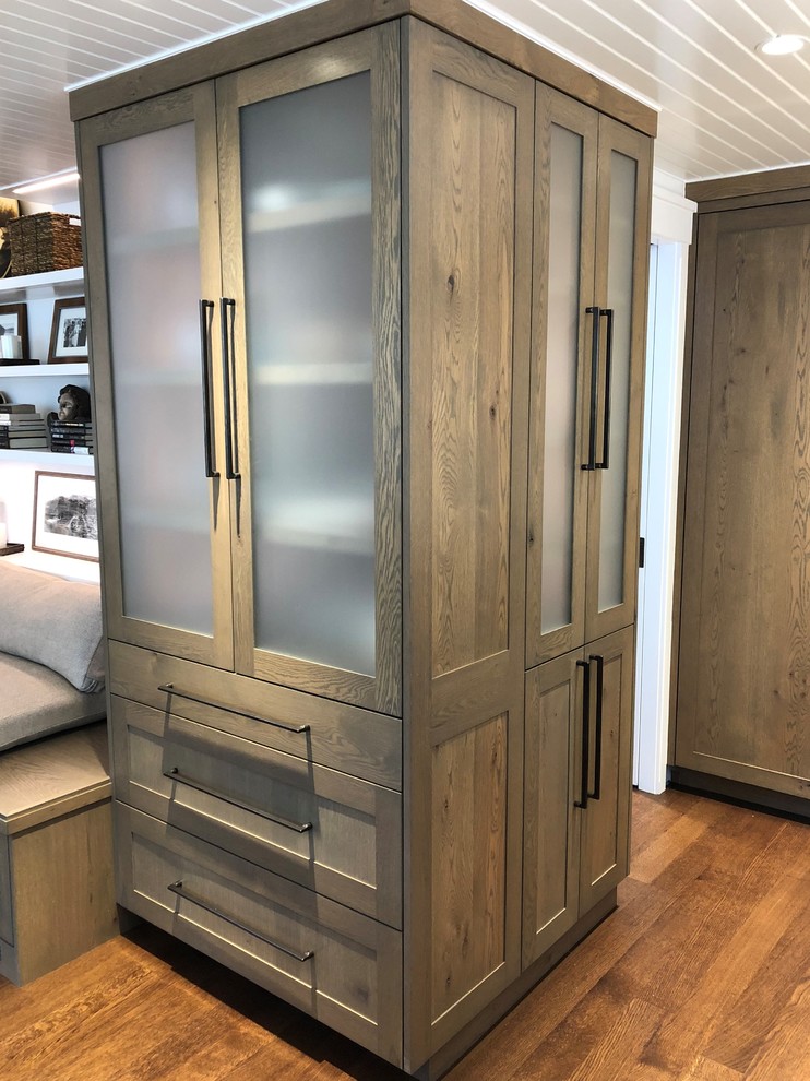 Diseño de armario unisex actual pequeño con armarios tipo vitrina, puertas de armario de madera clara, suelo de madera en tonos medios y suelo marrón