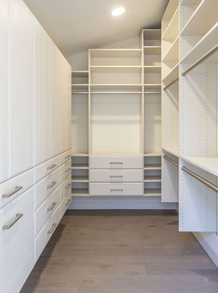 Diseño de armario vestidor unisex moderno grande con armarios con paneles lisos, puertas de armario blancas, suelo de madera en tonos medios y suelo gris