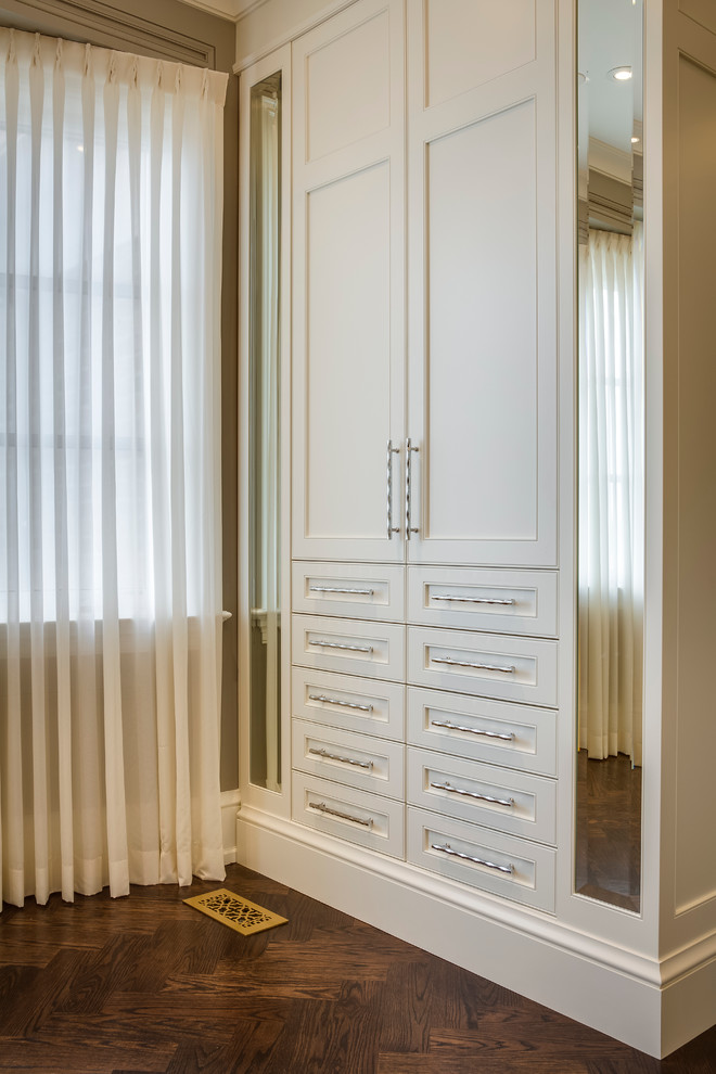 Diseño de vestidor unisex moderno de tamaño medio con puertas de armario blancas, suelo de madera en tonos medios y armarios con paneles empotrados