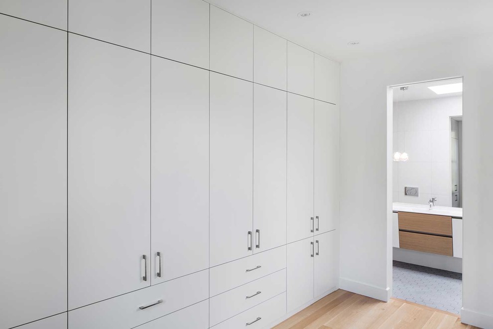 Foto de armario unisex actual grande con armarios con paneles lisos, puertas de armario blancas y suelo de madera en tonos medios