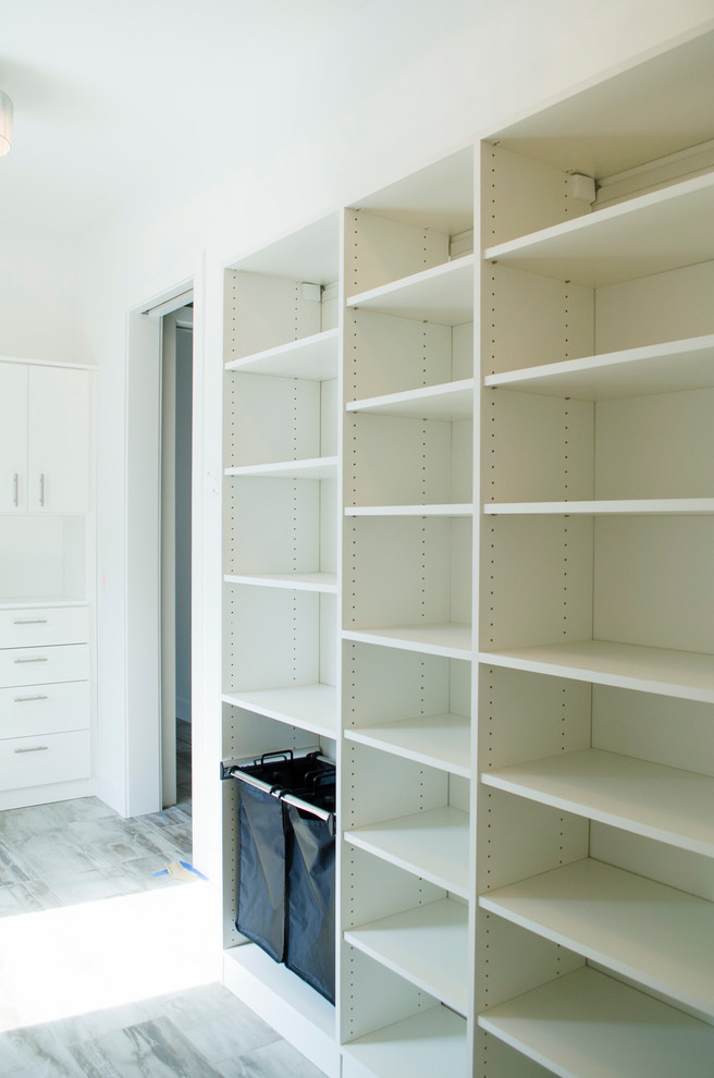 Ejemplo de armario vestidor unisex actual grande con armarios con paneles lisos, puertas de armario blancas y suelo gris