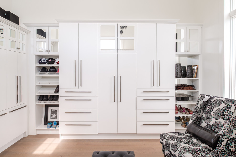 Diseño de vestidor unisex costero grande con armarios con paneles lisos, puertas de armario blancas y suelo de madera clara