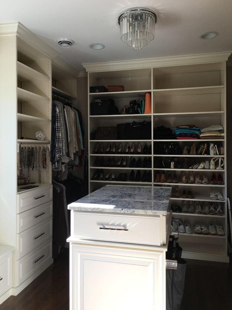 Ejemplo de armario vestidor unisex clásico de tamaño medio con armarios con paneles con relieve, puertas de armario blancas y suelo de madera oscura