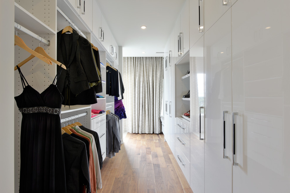 Modelo de armario vestidor unisex actual grande con armarios con paneles lisos, puertas de armario blancas, suelo de madera en tonos medios y suelo marrón