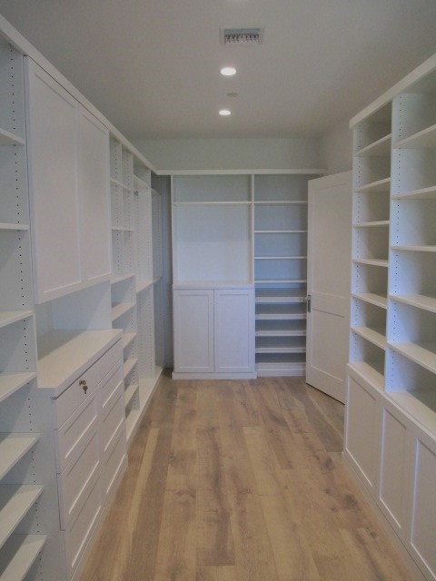 Ejemplo de armario vestidor unisex costero grande con armarios estilo shaker, puertas de armario blancas y suelo de madera clara