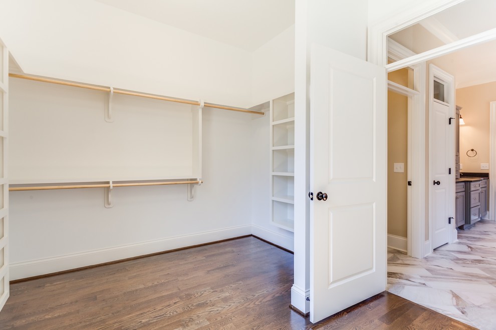 Idée de décoration pour un grand dressing room tradition neutre avec un placard sans porte, des portes de placard blanches et un sol en bois brun.