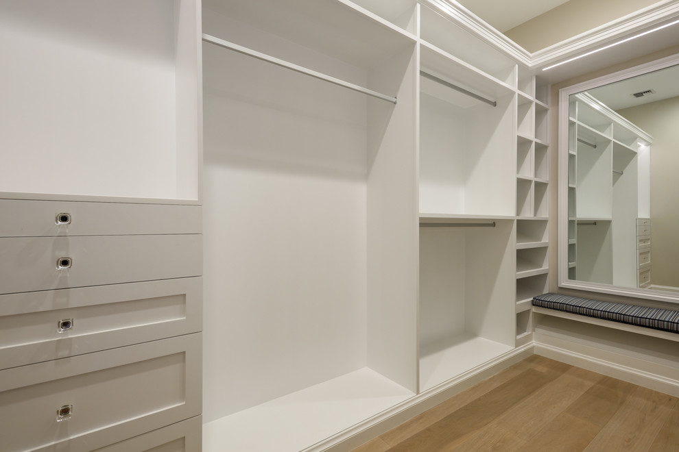 Imagen de armario vestidor unisex clásico renovado grande con armarios estilo shaker, puertas de armario blancas y suelo de madera clara