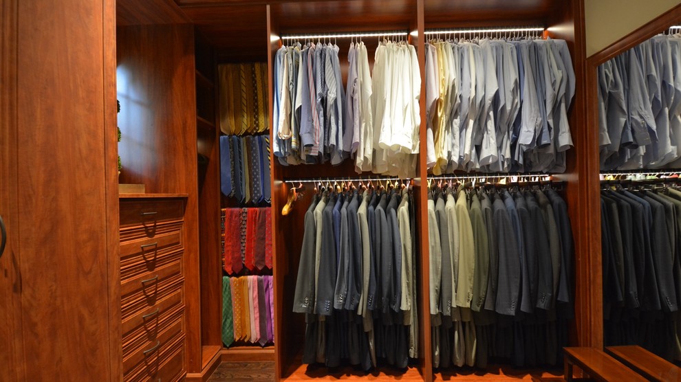 Ejemplo de armario vestidor de hombre tradicional de tamaño medio con armarios con paneles con relieve, puertas de armario de madera oscura y suelo de madera oscura