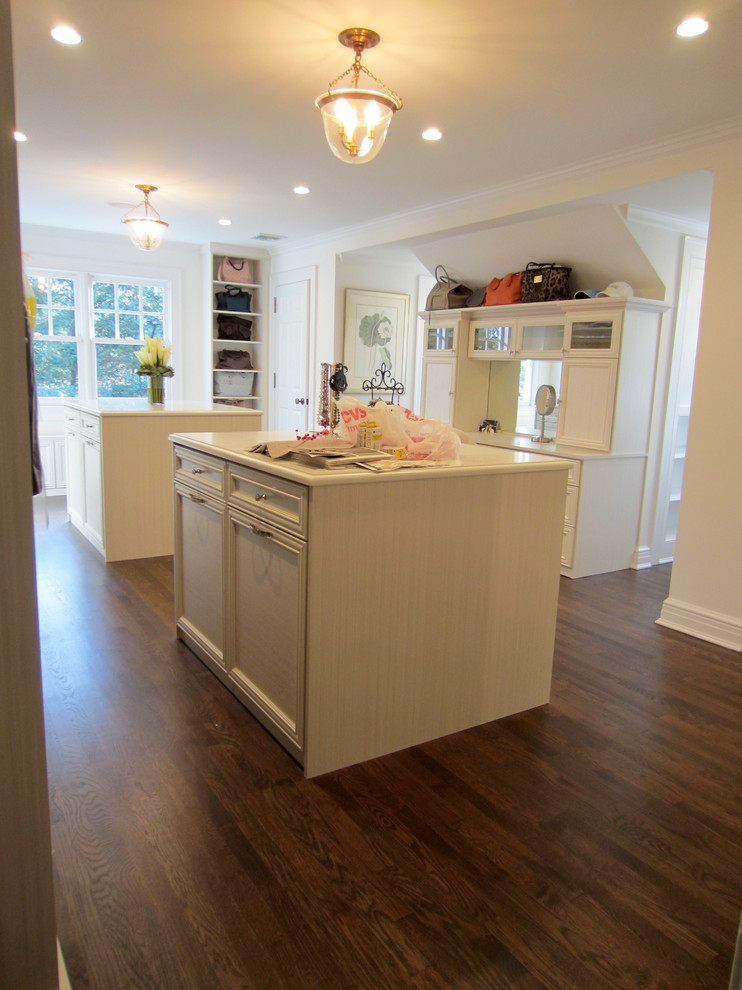 This is an example of a medium sized traditional walk-in wardrobe for women in New York with raised-panel cabinets, white cabinets and dark hardwood flooring.
