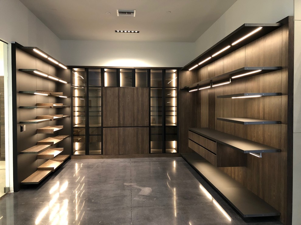 Imagen de armario vestidor unisex actual grande con armarios con paneles lisos, puertas de armario de madera oscura, suelo de cemento y suelo negro