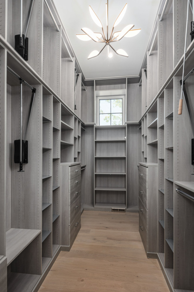 Diseño de armario vestidor de mujer y abovedado moderno grande con armarios con paneles lisos, puertas de armario grises, suelo de madera clara y suelo beige