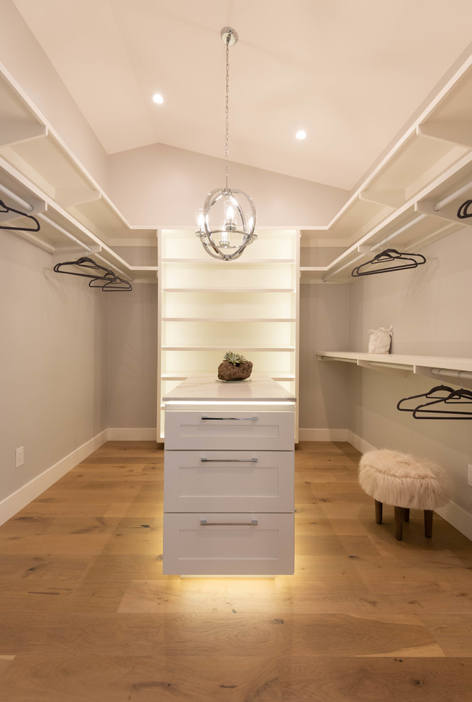 Cette image montre un dressing minimaliste de taille moyenne et neutre avec un placard à porte shaker, des portes de placard blanches et un sol en bois brun.